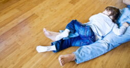 A young girl with braids, lying on her father's lap as they take a nap on their bamboo, hardwood flooring.