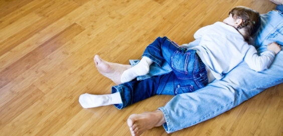 A young girl with braids, lying on her father's lap as they take a nap on their bamboo, hardwood flooring.
