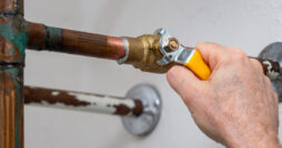 A close-up view of a hand using a wrench to tighten the valve of a household’s water shut-off system.