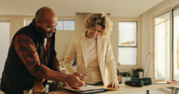 A home renovation professional signing a contract with a homeowner while sitting at a table with a contract.
