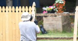 A worker wearing protective clothing for outdoor garden work. He is installing a wooden fence using nails and a hammer.