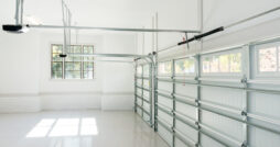 A large, empty garage consists of white walls, epoxy flooring, a window, and two closed steel garage doors.