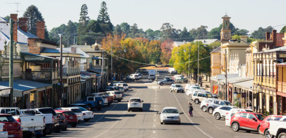 Vehicles parked on a busy street filled with businesses. Other vehicles drive down the road, and people cross the street.