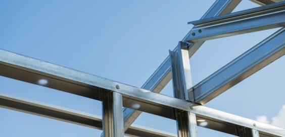 A close-up of an assembled portion of steel framing for a home set against a clear blue sky.