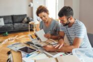 Man and woman sitting behind a table looking at different sample booklets inside a home living room with a couch.