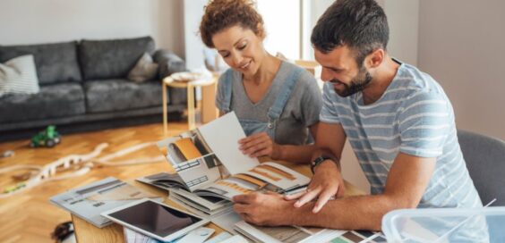 Man and woman sitting behind a table looking at different sample booklets inside a home living room with a couch.