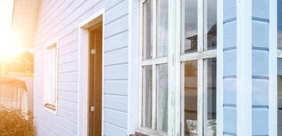 A close-up of a small dwelling unit with blue siding, white rustic windows, and an open brown front door.