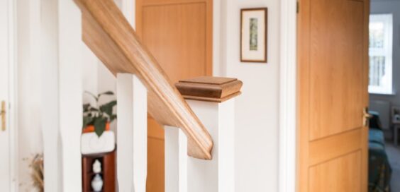 A close-up of a wooden staircase handrail inside a home with white painted walls and warm wood accents.