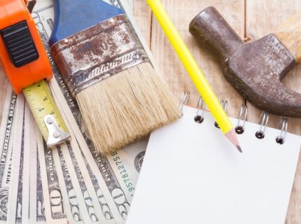 An overhead view shows money, a calculator, a notebook, and tools to plan and budget for home remodeling.