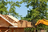 An industrial telehandler lifts a stack of plywood up to the level of the roof during a home's construction.