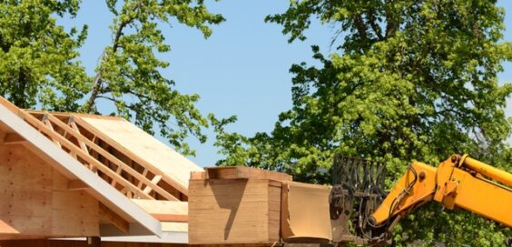 An industrial telehandler lifts a stack of plywood up to the level of the roof during a home's construction.
