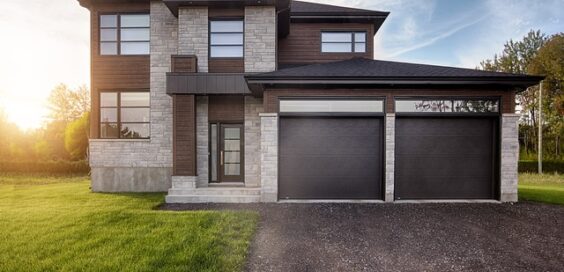 A modern home with a gray brick facade, brown siding, black garage doors, and a freshly paved driveway.