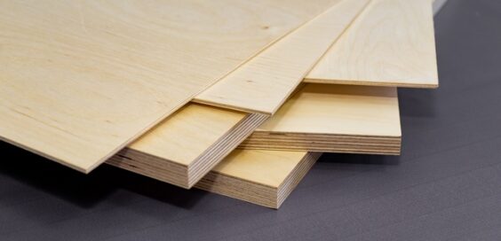 A close up of the corner of a stack of plywood. There are various styles and thicknesses of plywood on a gray surface.