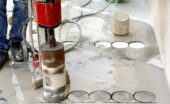 A close-up of an industrial worker using an industrial coring machine to core into a slab of wet concrete.