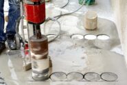 A close-up of an industrial worker using an industrial coring machine to core into a slab of wet concrete.