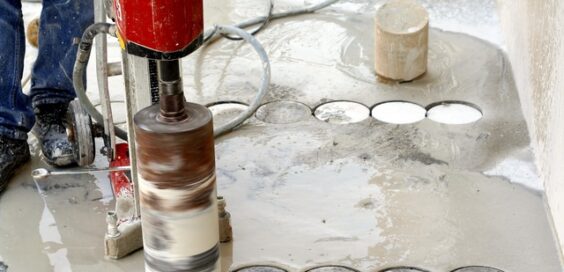 A close-up of an industrial worker using an industrial coring machine to core into a slab of wet concrete.
