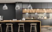 A modern kitchen with black cabinets, gray tile backsplash, and a wooden kitchen island with teacups on it.