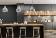 A modern kitchen with black cabinets, gray tile backsplash, and a wooden kitchen island with teacups on it.