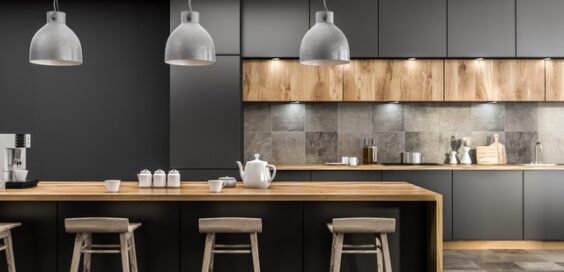 A modern kitchen with black cabinets, gray tile backsplash, and a wooden kitchen island with teacups on it.
