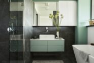 A small minimalist bathroom features a white tub, black shower surround, green walls, cabinetry, and accents.