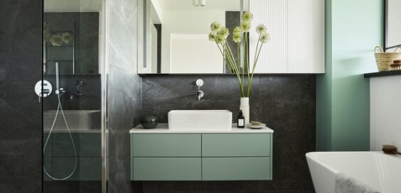 A small minimalist bathroom features a white tub, black shower surround, green walls, cabinetry, and accents.