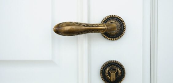 A white wooden door with an ornate handle doorknob. A lock mechanism is beneath it. Both fixtures are made of bronze.