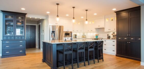 A bright, modern kitchen with white and black cabinets. An island in the middle has black cabinetry and white counters.