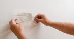 A person applying a mesh repair patch over drywall with both hands. There is a deep hold inside the drywall.