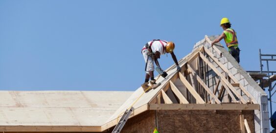 Two men in brightly colored safety gear work on a residential roof with exposed wood beams and visible roof decking.