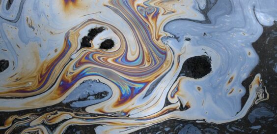 A close-up of oil mixed into water on the ground, showing abstract colors along with rocks and dirt.