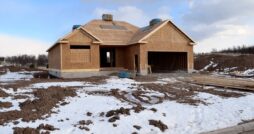 A new home under construction on a muddy plot of land that is covered with snow.