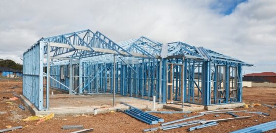 A house that is in the process of being built on an empty lot appears to have a frame made out of a blue colored metal.