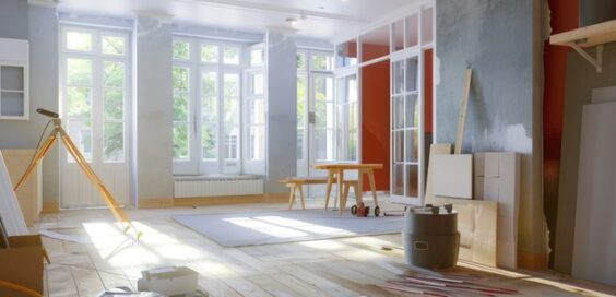 A spacious room with wood floors and large windows. Tools are scattered across the room, and the walls are unfinished.