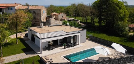 Aerial view of a modern large house with a flat roof, swimming pool, and patio on a large plot of land.
