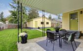 A landscaped backyard of someone's yellow, mid-century modern home with a matching detached guest house.