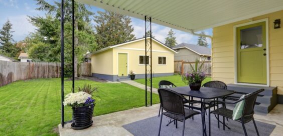 A landscaped backyard of someone's yellow, mid-century modern home with a matching detached guest house.