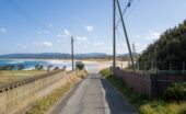An empty side street near a beach with utility poles overhead. There are fences along the paved street.
