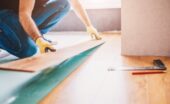 Person installs laminate flooring at home, fitting planks carefully as they finish the last section of the room.