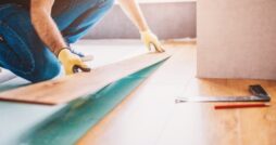 Person installs laminate flooring at home, fitting planks carefully as they finish the last section of the room.