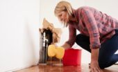 A woman using a sponge to mop up a large puddle that has come from a hole in the wall, exposing the plumbing within.