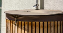 A close-up of a rainwater harvesting barrel stored outside a home with a metal downspout leading down from the roof.