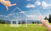 A pair of hands framing a house sketch that has been overlaid on a backdrop of an open section of land.