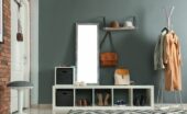 The mudroom of a home with grey and red brick walls, storage for shoes, a coat rack, a mirror, and hardwood floors.