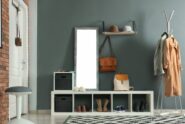 The mudroom of a home with grey and red brick walls, storage for shoes, a coat rack, a mirror, and hardwood floors.