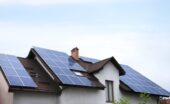 A residential home with rooftop solar panels mounted across multiple roof sections beneath a bright sky.