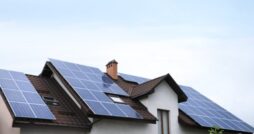 A residential home with rooftop solar panels mounted across multiple roof sections beneath a bright sky.