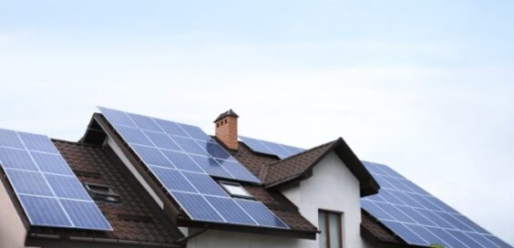 A residential home with rooftop solar panels mounted across multiple roof sections beneath a bright sky.