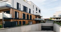 Modern apartment buildings with white walls, wood cladding, glass balconies, and underground garage ramp.