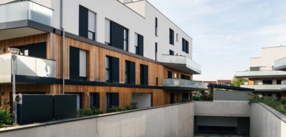 Modern apartment buildings with white walls, wood cladding, glass balconies, and underground garage ramp.