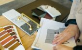 A designer reviewing samples for a kitchen design, with cabinet color swatches and gold handles on a table.